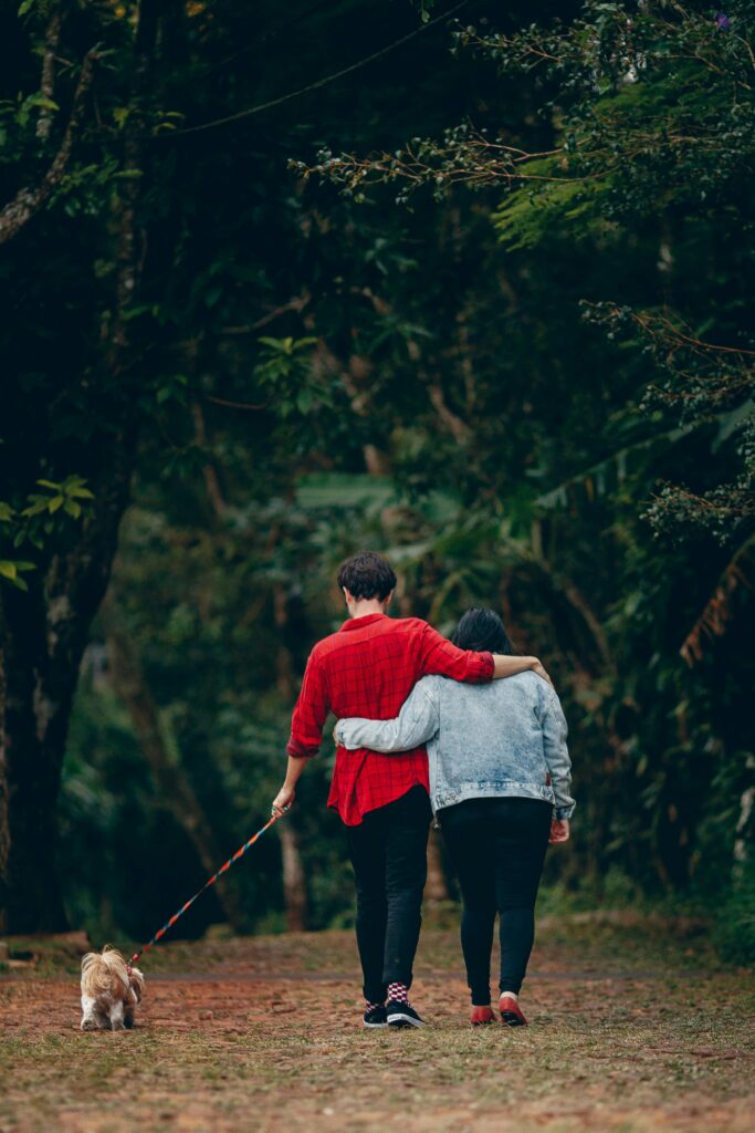 A romantic couple embraces and walks their dog in a lush, green park.