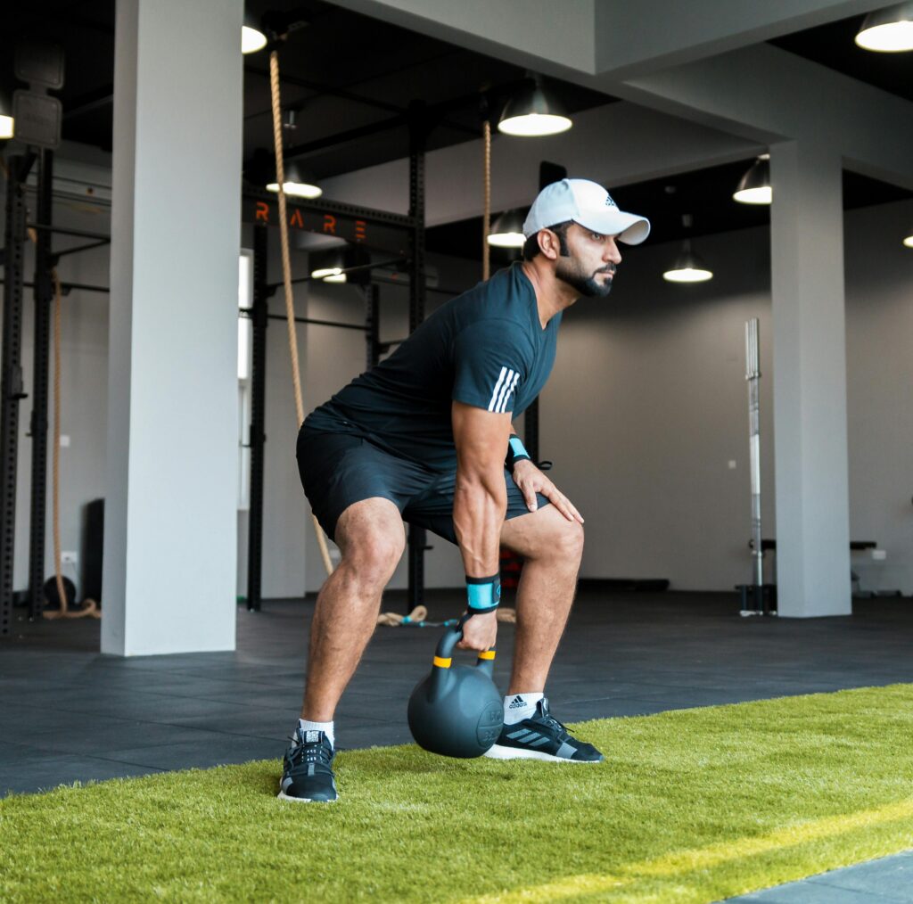A man in activewear performs a kettlebell swing in a modern gym setting.